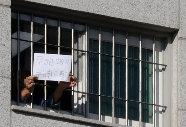 지난 6일 서울 송파구 서울동부구치소에서 한 수용자가 문재인 대통령과 법무부를 비판하는 내용의 종이를 창문 밖으로 내밀고 있다. (사진=뉴시스)