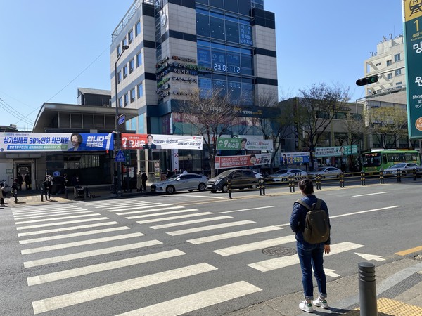 (한 시민이 신호를 기다리며 후보자들의 현수막을 보고 있다 사진=조유라)