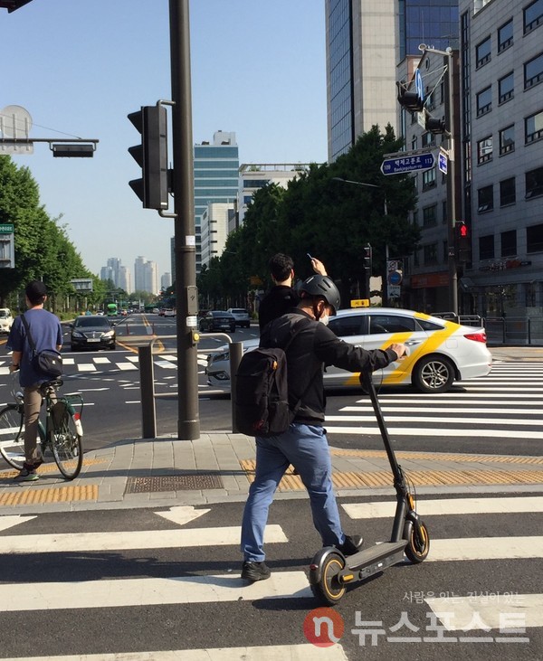 13일 오전  헬멧을 쓴 한 전동킥보드 이용자가 횡단보도를 걸어서 이동하고 있다. (사진=뉴스포스트 홍여정 기자)