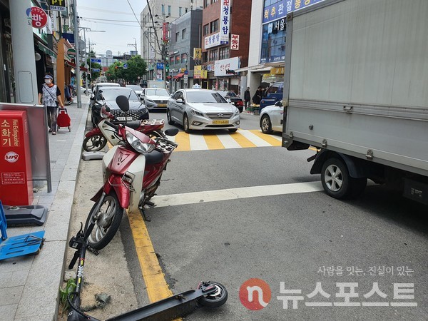 방학 도깨비시장 2문과 3문 사이 도로에 주청차된 차량과 오토바이, 쓰려져 있는 킥보드. (사진=뉴스포스트 이해리 기자)