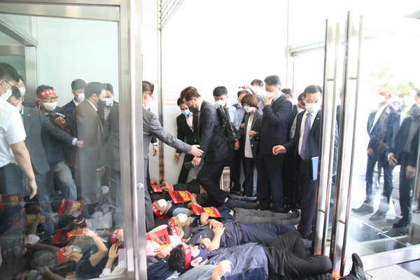 산업은행 강석훈 회장이 21일 오전 서울 여의도 본점 정문 앞에 드러누워 있는 노동조합 간부들을 피해 출근을 강행하고 있다. (사진=전국금융산업노동조합 한국산업은행지부)