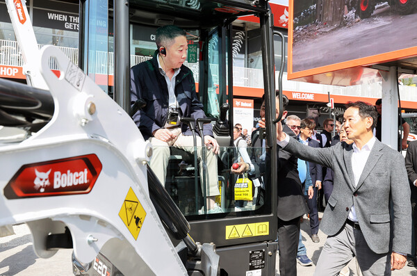 박정원 두산그룹 회장(왼쪽)이 바우마 2025에서 두산밥캣의 유럽시장 주력인 미니굴착기 신제품에 탑승해 스캇 박 두산밥캣 부회장(오른쪽)의 설명을 듣고 있다. (사진=두산그룹)